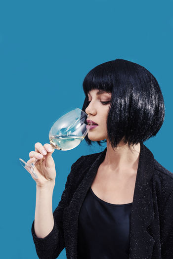 Young woman drinking wine in glass against blue background