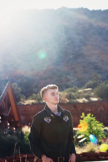 Young man looking away while standing against mountains during sunny day