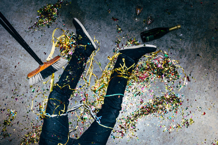 Top view of crop anonymous male lying on floor with colored paper streamers and bottle of champagne during festive occasion