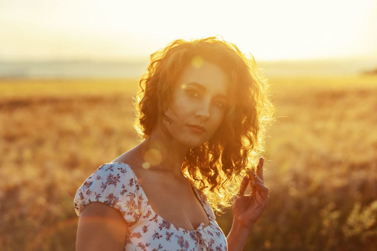 Young moroccan woman, with brown curly hair,  in wheat field,  sunset blinding the camera