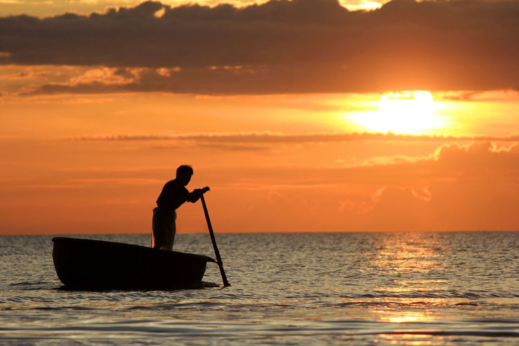 Silhouette man in boat on sea against sky during sunset