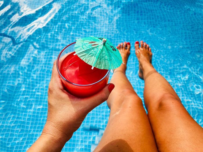 Low section of woman holding drink glass at swimming pool