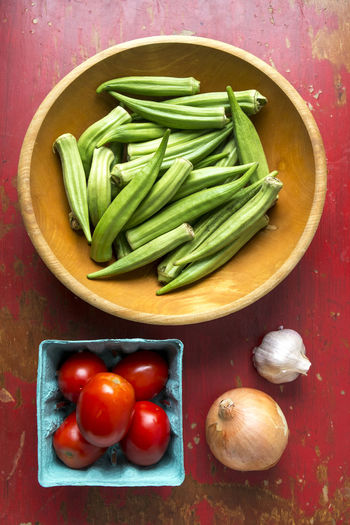 Ingredients for pan seared okra and tomatoes on a red table