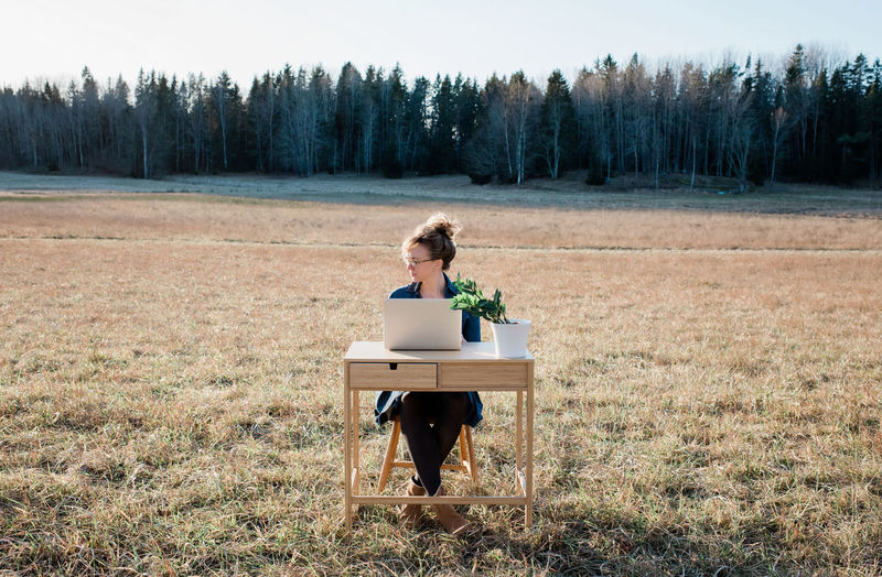 Travelling woman working on a desk and laptop in a field at sunset