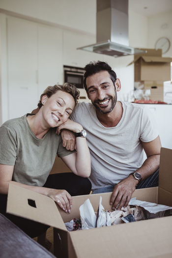 Portrait of smiling male and female partners unpacking cardboard boxes in new house