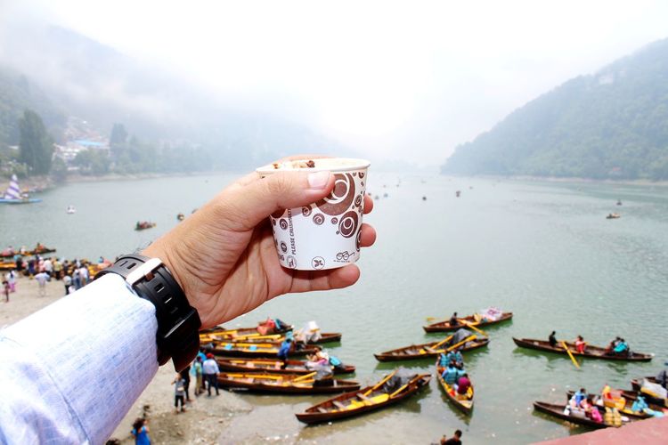 Close-up of hand holding disposable cup over boats on river