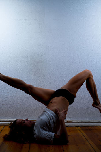 Side view of woman practicing shoulder stand against white wall