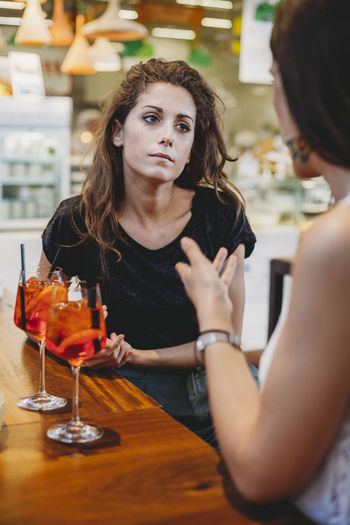 Female friends with aperitifs on table talking while sitting in restaurant