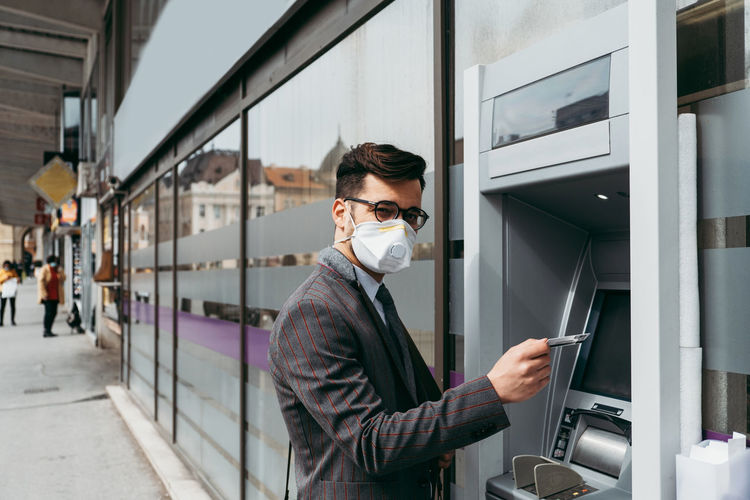 Business man with protective face mask using street atm machine.