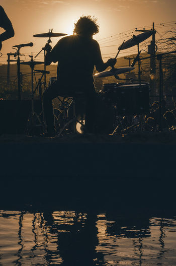 Rear view of silhouette drummer playing cymbal during sunset