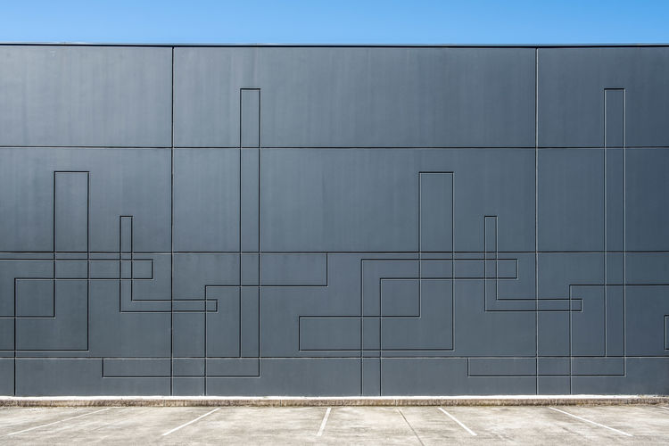 Dark gray concrete wall of industrial building with geometric pattern with empty parking spaces