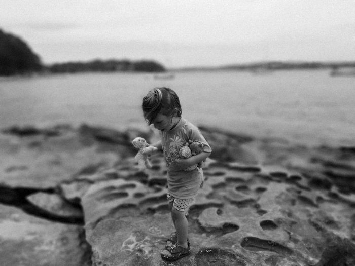 Cute girl holding toys while standing on rock at beach