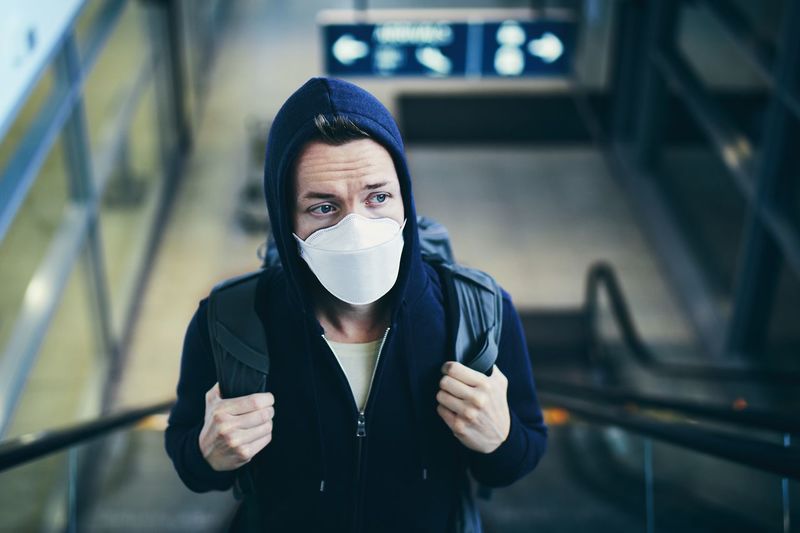 Man wearing mask looking away while standing on escalator at airport