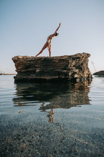 Ballet dancer dancing on rock in sea against clear sky
