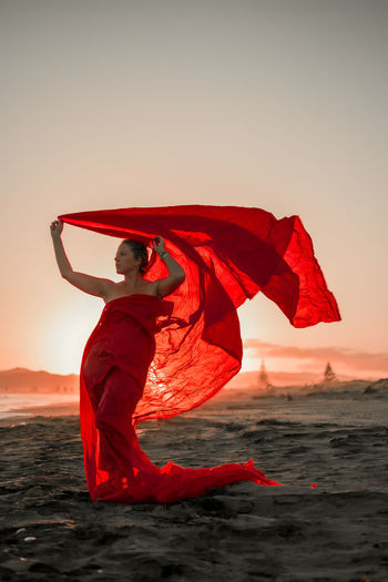 Woman with red umbrella at beach against sky during sunset