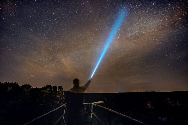 Digital composite image of man holding flashlight against star field