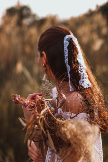 Portrait of brunette women in a white blouse and ribbon with a bouquet of dried flowers in the field 