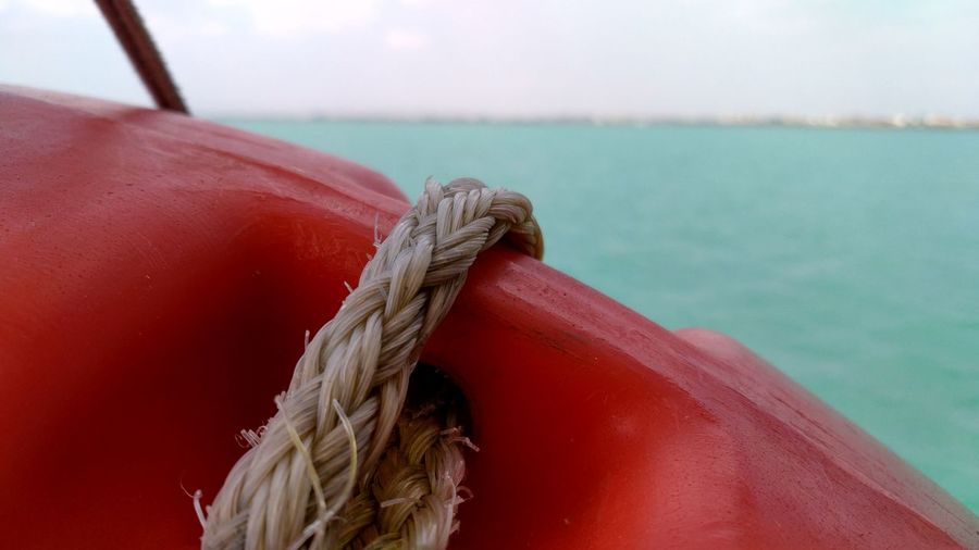 Close-up of rope tied with life belt on boat against sea and sky