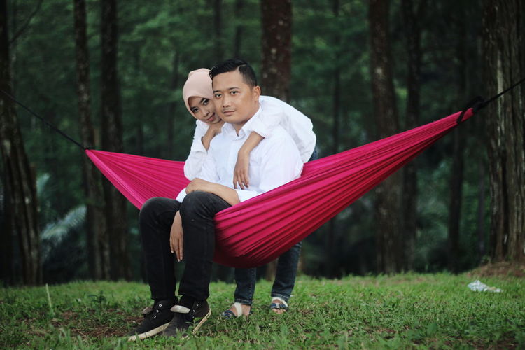 Portrait of woman with boyfriend sitting on hammock in forest