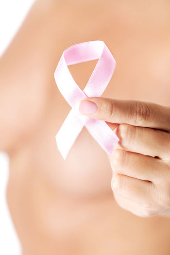 Midsection of shirtless woman holding breast cancer awareness ribbon against white background