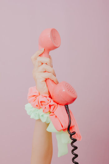 Close-up of hand holding telephone receiver against pink background