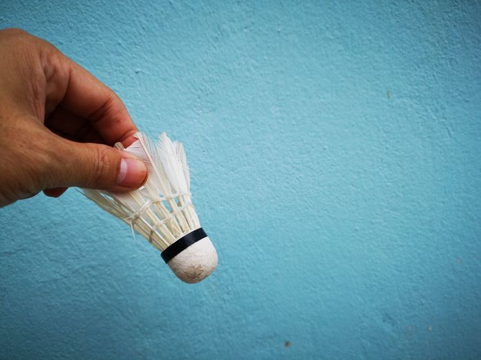 Cropped hand holding shuttlecock against wall