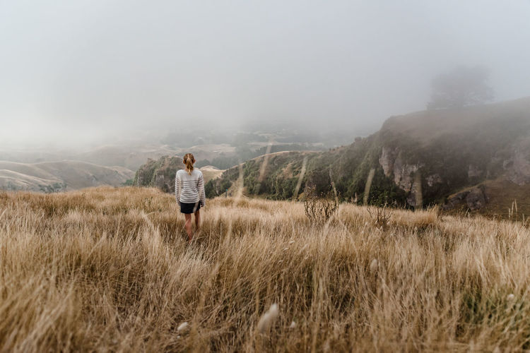Girl walking through tall grass on a foggy morning in new zealand