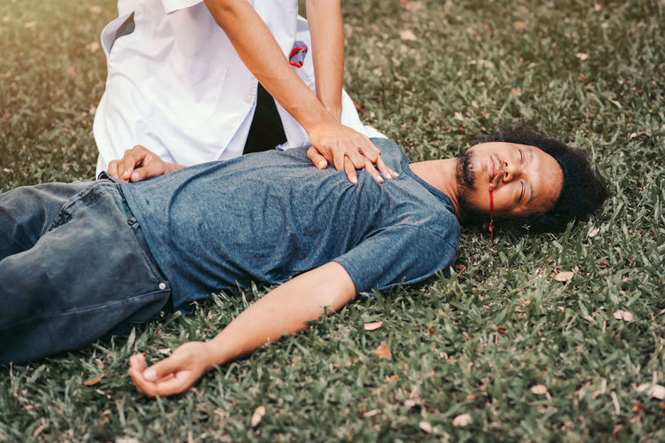 Midsection of doctor performing car on patient lying down at grass outdoors