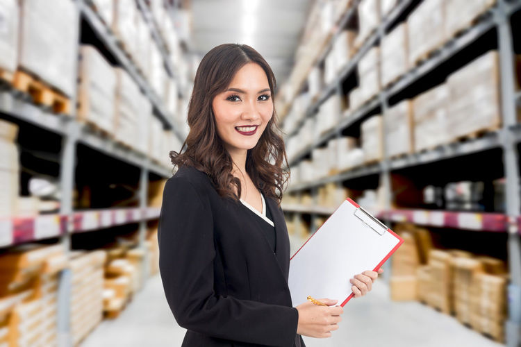 Portrait of smiling worker with clipboard standing in warehouse