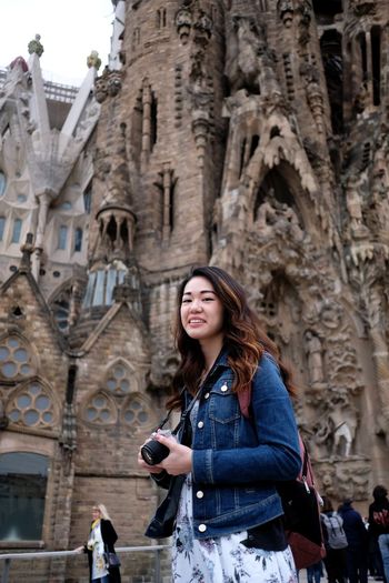 Portrait of smiling young woman standing against building in city