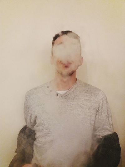Young man exhaling smoke against wall