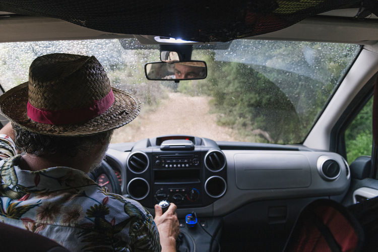 A man in a hat drives a car on a dirt road. rear view. vacation concept person