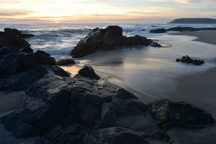 Rocks on sea shore against sky during sunset