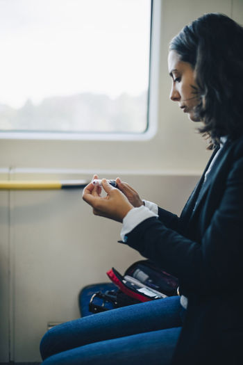 Woman looking at injection pen while sitting by window in train
