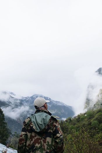 Rear view of man looking at mountains against sky