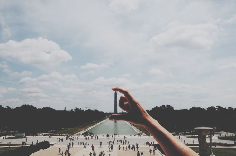 Optical illusion of man holding washington monument against sky