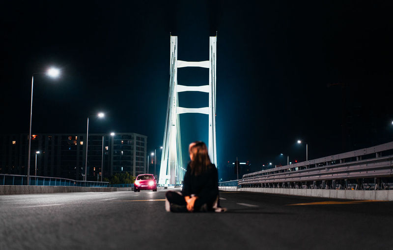 Young woman sitting on city road at night