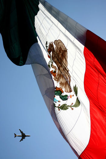Low angle view of airplane by mexican flag against sky