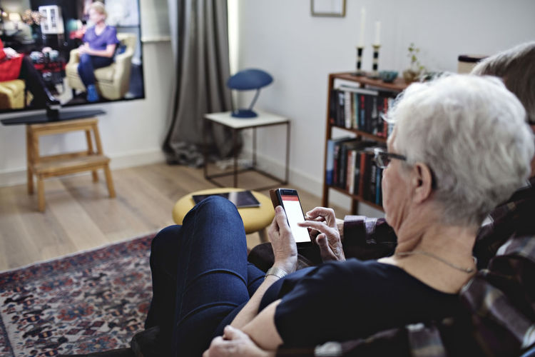 High angle view of senior couple sitting with smart phone watching tv at home
