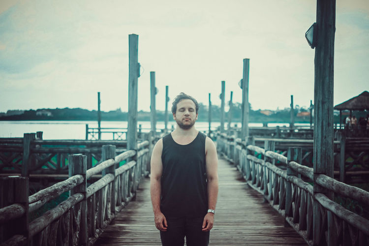 Portrait of man standing on footbridge against sky, dramatic, reflexive