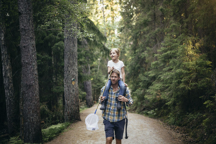 Father carrying daughter on shoulder while walking in forest