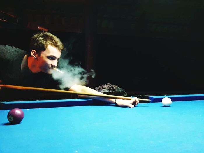 Man smoking cigarette while playing pool