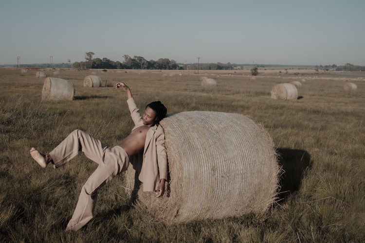 Full length of young man falling on hay bale at agricultural landscape