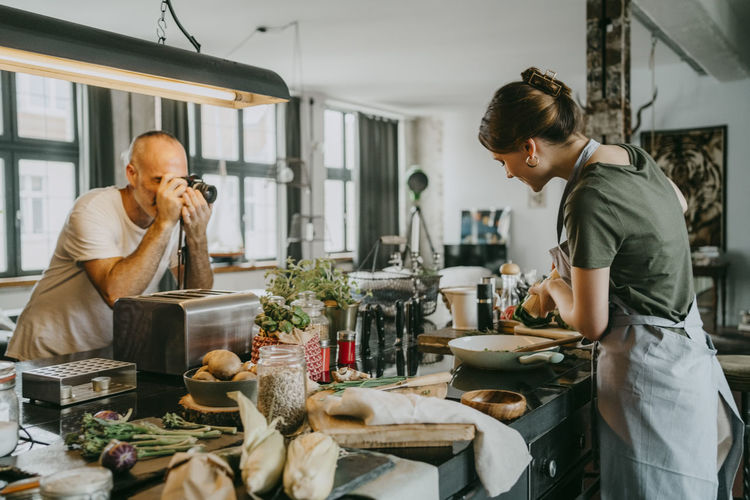 Photographer clicking picture of chef preparing food in studio kitchen