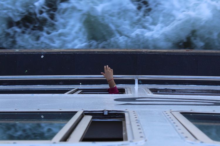 Cropped hand of person at window in ferry on sea