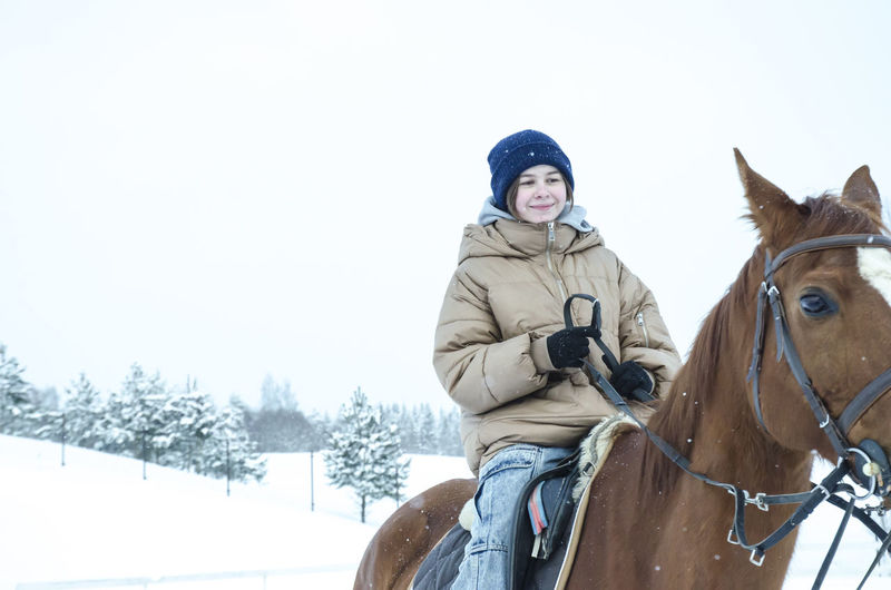 Woman riding horse on snow covered field against clear sky