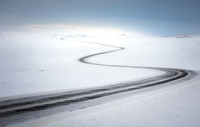 Empty curvy country road going through desert snowy terrain in cold winter day with blue sky in iceland