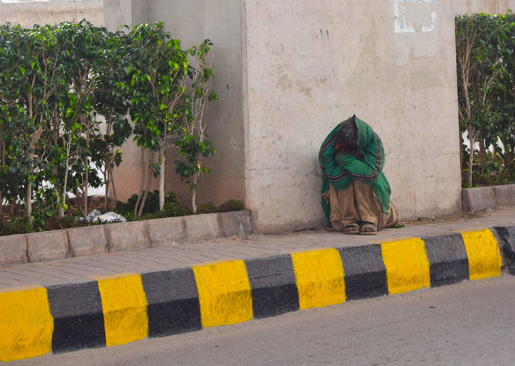 Man covered with shawl sitting on footpath