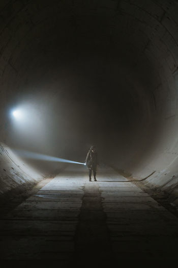 Person with flashlight illuminating darkness and exploring grungy underground tunnel with concrete walls during apocalypse