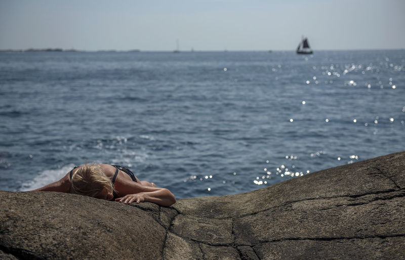Young woman lying on rocks by sea against sky